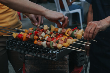 People are cooking seafood and vegetable skewers on a charcoal grill. with a plate of shrimp placed next to it A warm family holiday celebration. BBQ party