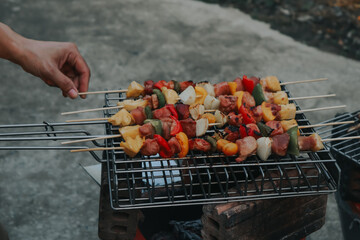 People are cooking seafood and vegetable skewers on a charcoal grill. with a plate of shrimp placed next to it A warm family holiday celebration. BBQ party