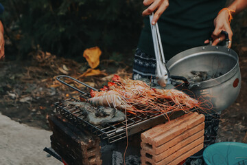 Fototapeta premium People are cooking seafood and vegetable skewers on a charcoal grill. with a plate of shrimp placed next to it A warm family holiday celebration. BBQ party