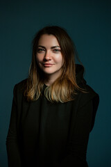 Classic dark studio portrait of a young brown-haired woman in black clothes sitting on a chair.