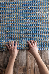 Man rolling hand woven geometric denim area rug on a wooden floor at home.