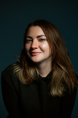 Classic dark studio portrait of a young brown-haired woman in black clothes sitting on a chair.