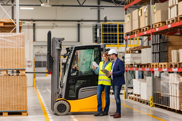 Female forklift driver, warehouse worker talking with manager, standing by forklift. Warehouse...