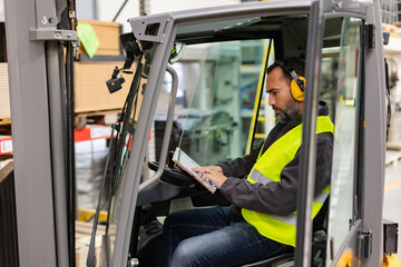 Warehouse worker driving forklift. Forklift driver reading order, order picking. Warehouse worker preparing products for shipmennt, delivery, checking stock in warehouse.