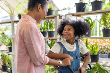 African mother and daughter is choosing tropical fern and ornamental plant from the local garden...