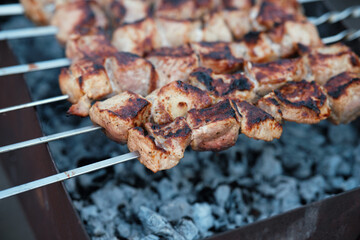 Lots of metal skewers with meat cooking on coals. Cooking pork barbecue.