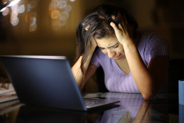 Sad woman complaining alone cheking laptop in the night - obrazy, fototapety, plakaty
