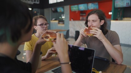 a group of students sit in a cafe lifestyle and do a project on a laptop together. business concept of modern training and development. students discuss their homework and eat fast food burgers