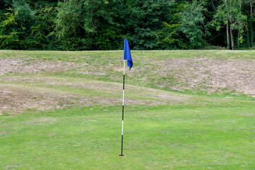 Obraz premium Close up view of the flagstick or pin with blue fabric on the green of a golf course with trees in the background