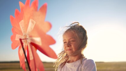 child girl looking at the windmill a toy in the park. happy family childhood dream concept. daughter girl playing with a toy windmill in nature. childhood freedom wind concept outdoors lifestyle