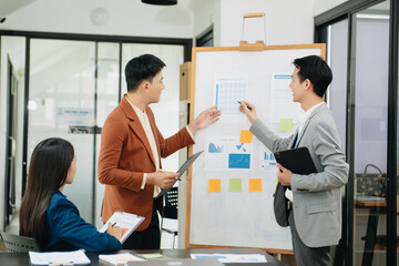 Fototapeta premium Mid age Asian business woman ceo executive manager showing to colleagues team income revenue data figures planning on big screen in modern office.