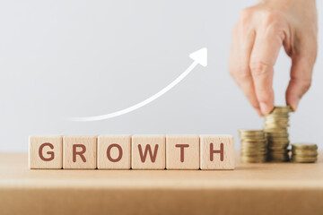 Business success growing growth increase up concept. Wooded cube block  with word GROWTH and increasing graph, blurred hand arranged stack of coins