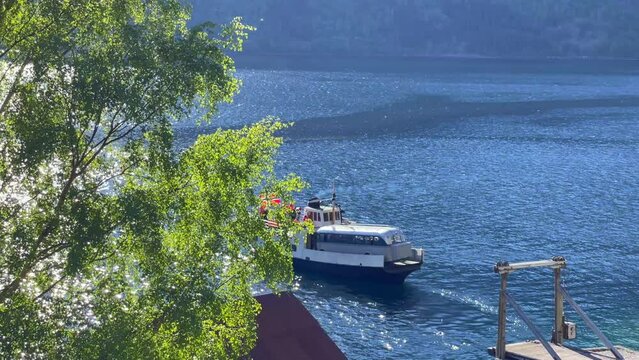 An old ferry departs from the quay in beautiful Eikesdal in Molde municipality. The ferry has an old bus on board and a few passengers. The ferry operates on Eikesdalsvatnet.