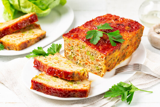 Homemade meatloaf or terrine with mix of chicken and turkey meat, carrot, leek and green peas, glazed with ketchup. Baked minced chicken meat. White table surface, vertical image.