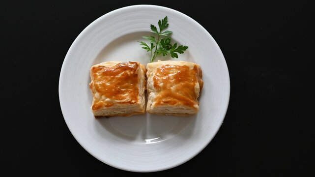 2 quadratische gef&uuml;llte Bl&auml;tterteigtaschen mit Petersilie garniert auf einem weissen Teller angerichtet