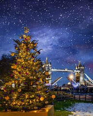 A illuminated Christmas Tree in front of the famous Tower Bridge of London, England, with snow...