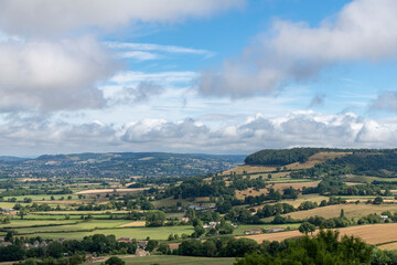 Panoramic view over the hilly landscape on the Cotswolds edge near Dursley, Gloucestershire, UK along the public footpath of Cotswold Way against a white clouded blue sky