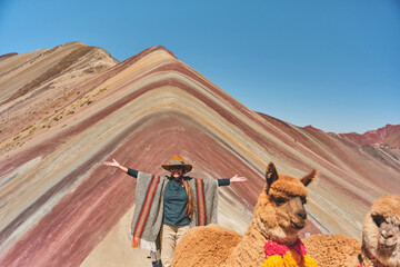 Woman standing and alpaca in the rainbow mountain in Peru with all the colors of the mountain in the background.