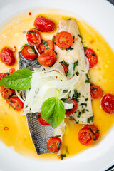 unpeeled fish with gravy, herbs, cherry tomatoes and onions, top view