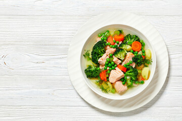 salmon, veggies and green herbs soup in bowl