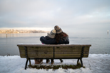 Embraced by Winter: Two young women sit on a snow-covered bench at Lake Constance