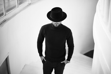 Stylish man in black with hat looking down.