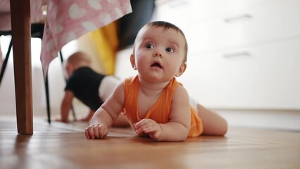 beautiful twin baby crawling under the kitchen table. carefree twins childhood. baby a boy funny...