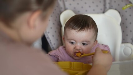 baby newborn eats. happy family dream weaning concept. dirty mess baby girl eating vegetables. baby daughter eats on a feeding chair indoors dirty face. naughty dirty babe indulges while feeding .