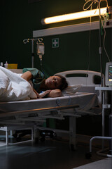 Girl in the hospital bed has a drip in her hand for medicine. She's receiving treatment and has a...