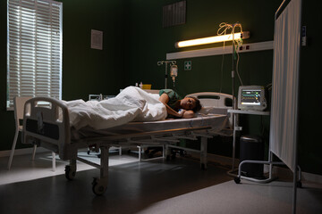 The girl is lying in a hospital bed, with catheter in her hand.