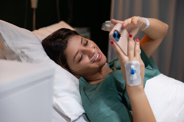 Young girl is lying in the ward, holding the phone in her hands, texting her boyfriend online while recovering in the hospital after a serious illness.