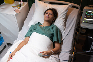 Young woman lies in a hospital bed after a severe accident. She is resting, surrounded by medical...