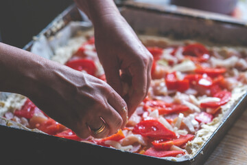 Preparing the Italian pizza. Chef's hands adding on a pizza tomatoes slice, parsley and basil....