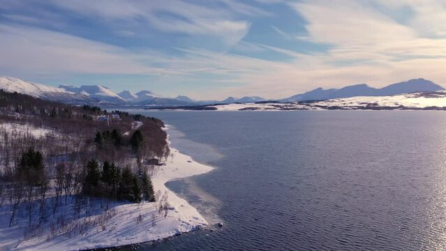Snow covered mountain range on coastline in winter, Norway. Surroundings of town Tromso. Panoramic aerial view landscape of nordic snow cowered mountains, houses and ocean. Troms county, Fjordgard