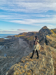 Fototapeta premium A woman on the background of the rocky coast of the Barents Sea. Beautiful view of the cliffs and the coast of the Rybachy and Sredny peninsulas. The harsh beauty of the north.