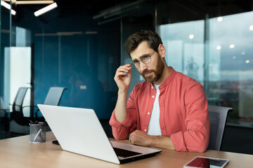 Naklejka premium Sad unhappy and disappointed man at workplace inside office, businessman in shirt and glasses unhappy with achievement results, accountant with bad statistical report.
