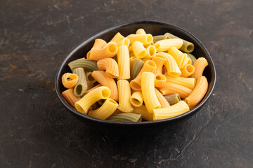 Rigatoni colored raw pasta with tomato, eggs, spices, herbs on black concrete. Side view.