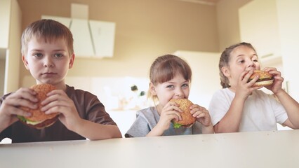 children eat burgers. fast food burger. a group of small children in the kitchen greedily eat fast...