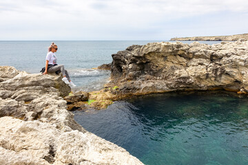 Fototapeta na wymiar The girl at Cape Tarkhankut. The rocky coast of the Dzhangul Reserve in the Crimea. Turquoise sea water. Rocks and grottoes of Cape Tarkhankut on the Crimean peninsula.