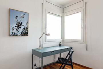 Desk with lamp and chair by corner windows in apartment - obrazy, fototapety, plakaty
