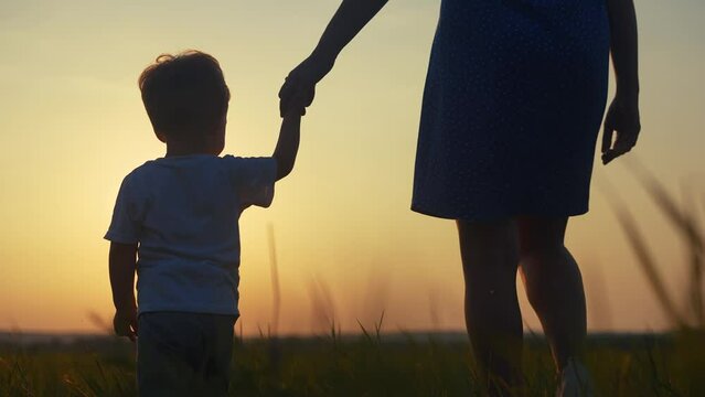 mom and son in the park. mom a holding her son hand walking in the park silhouette at sunset in nature. happy family kid lifestyle dream concept. mom and son family walking in nature