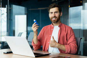 Joyful man with inhaler in hands smiling and looking at camera, showing thumbs up recommending...