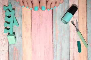 Summer pedicure. Girls toes with green nails, nail polish, nail file, and other pedicure accessories lying against a boho-style background. Summer nails beauty trends.