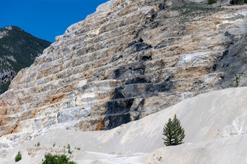 Fototapeta na wymiar Low angle view of industrial terraces in former quarry for limestone on the side of a mountain in BC, Western Canada containing calcium, magnesium carbonate or dolomite and limestone sand in front
