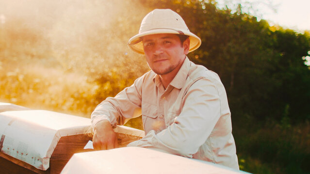 Close up portrait of attractive professional male beekeeper wearing special clothes looking at camera. Beautiful skillful man apicultural worker using bee smoker collecting honey. - Powered by Adobe