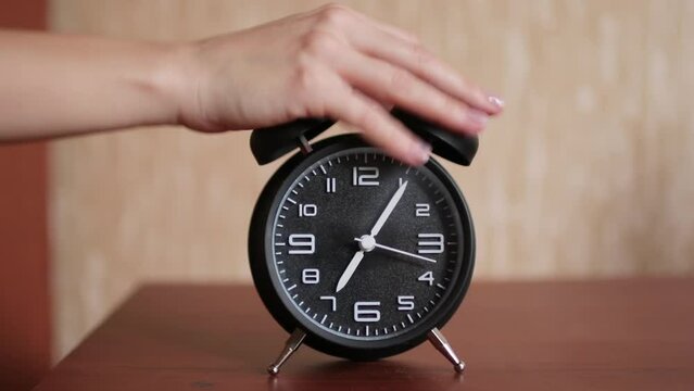 Old fashioned alarm clock ringing early in the morning. The woman's hand stops the alarm clock to sleep longer.