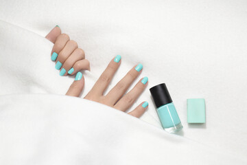 Mint manicure. Close-up of woman fingers with beautiful manicure, her hands are partially covered by white coverlet. Next to womans hands lays nail polish.