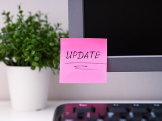 A pink paper notes with the reminder Update on it sticked on to a monitor at an office workplace.