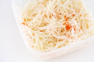 A plastic container full of salad with chopped cabbage and carrot. White background.