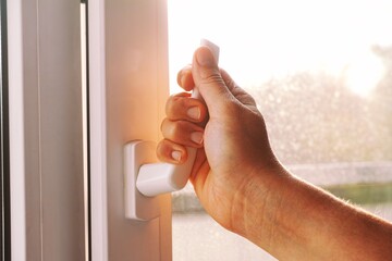 A woman opening a window using a window handle.